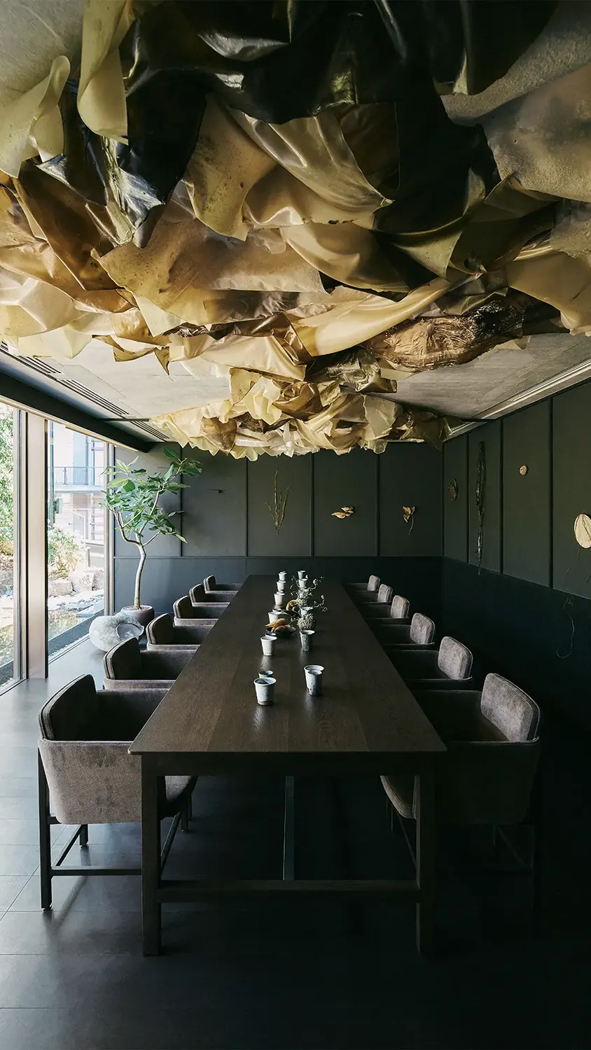 A private dining room with a long wooden table lined with chairs and cups lit by a contemporary lighting fixture