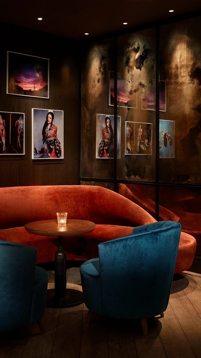 A moody corner in the lounge at 11 Howard hotel with a wooden table with an orange upholstered couch opposite two blue upholstered chairs