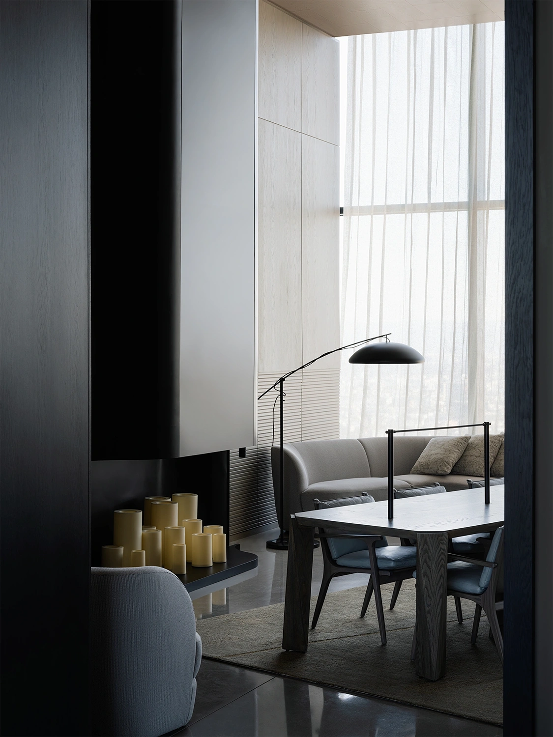 Well-lit hotel room featuring a expertly designed couch, table and chairs, and a candle fireplace, with natural light filtering through shaded windows.
