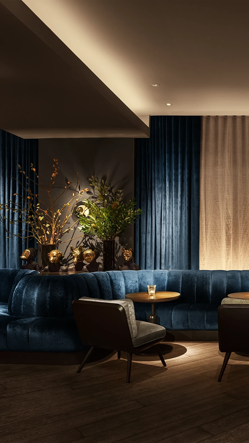 A lounge area inside a well-lit room with a blue upholstered couch seating a set of tables with opposing chairs